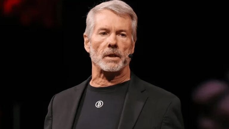 Michael Saylor speaking at a business event, with a screen showing company and token graphics behind him