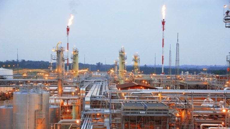 Gas flare burning at an oil field with mining containers nearby